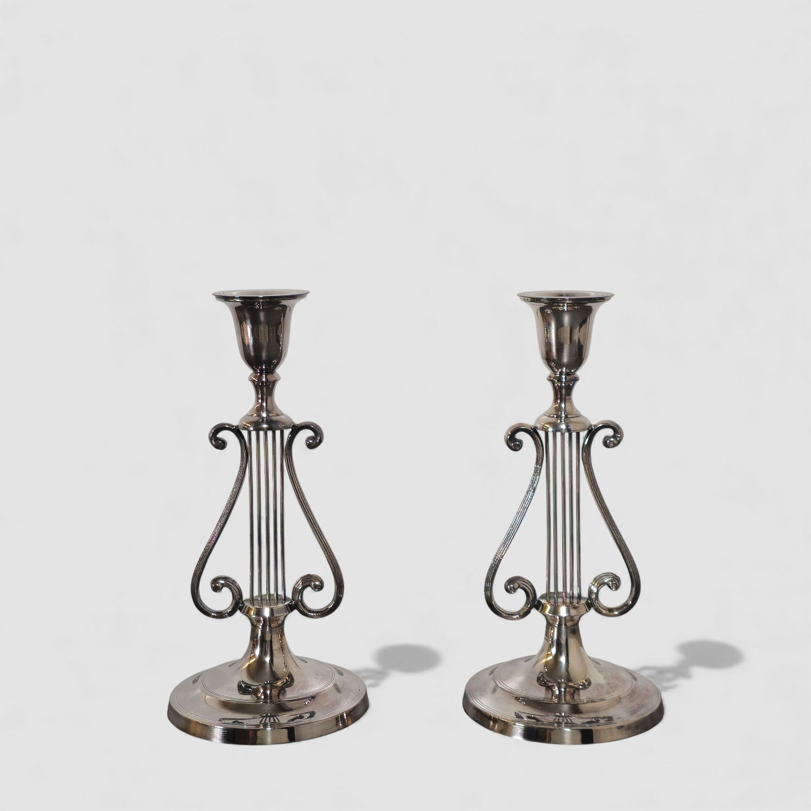 Lyre Form Silver on Brass Candlesticks: Lyre Form Silver on Brass Candlesticks. Pair. Circa 1940s. Scrolled lyres resting on an round footed base. 3 7/8 dia x 8 1/4h.