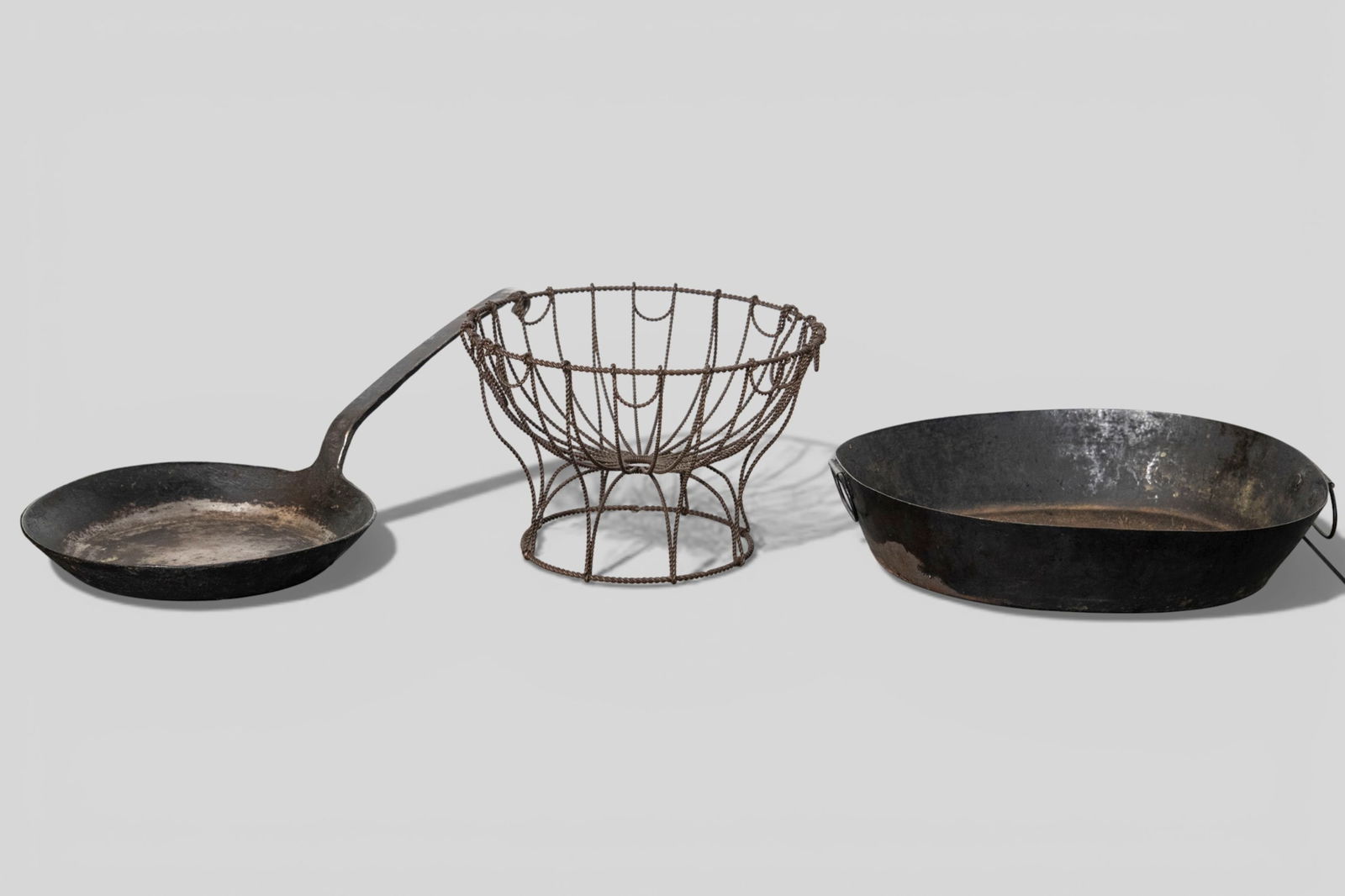 18th Century American Cookware: 18th Century American Cookware. 3 piece total. Unique braided tin fruit bowl. 9 dia x 6h. Oval enameled tin pan with loop handles. 12w x 10 1/2d x 2 5/8h; Enameled cast iron skillet with arched shoe