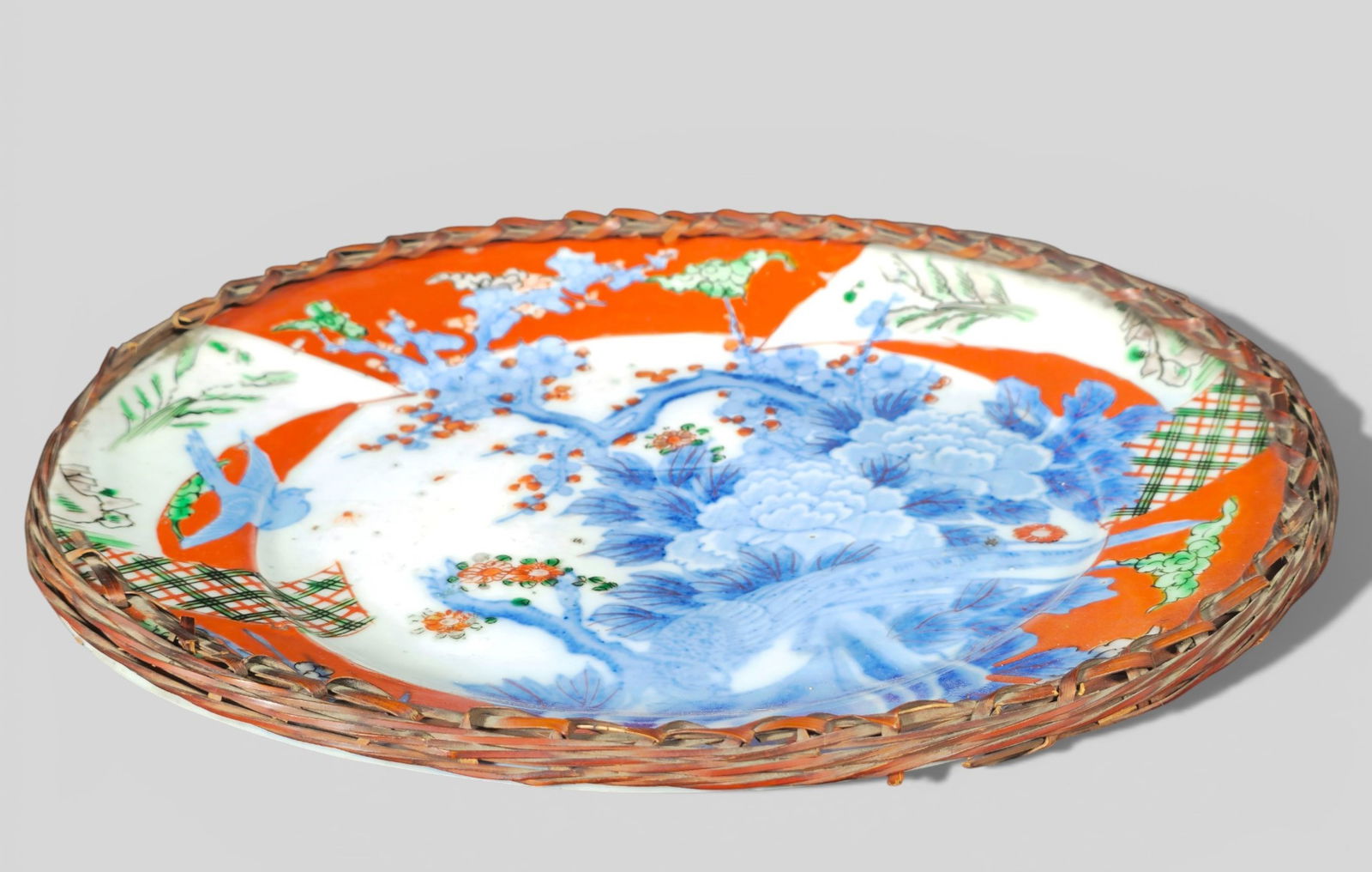Japanese Porcelain Serving Platter in Handmade Woven Basket Meiji Period: Japanese Porcelain Serving Platter in Handmade Woven Basket Meiji Period. Japanese porcelain serving platter from the Meiji period, decorated in a traditional palette and set within a handmade woven b