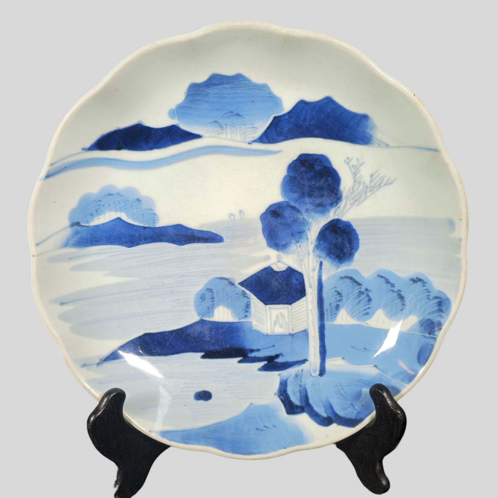 Asian Blue and White Charger with Scalloped Rim: Asian Blue and White Charger with Scalloped Rim. Finely painted blue and white charger featuring a serene landscape water scene with mountains, trees, and architectural elements, executed in soft cela