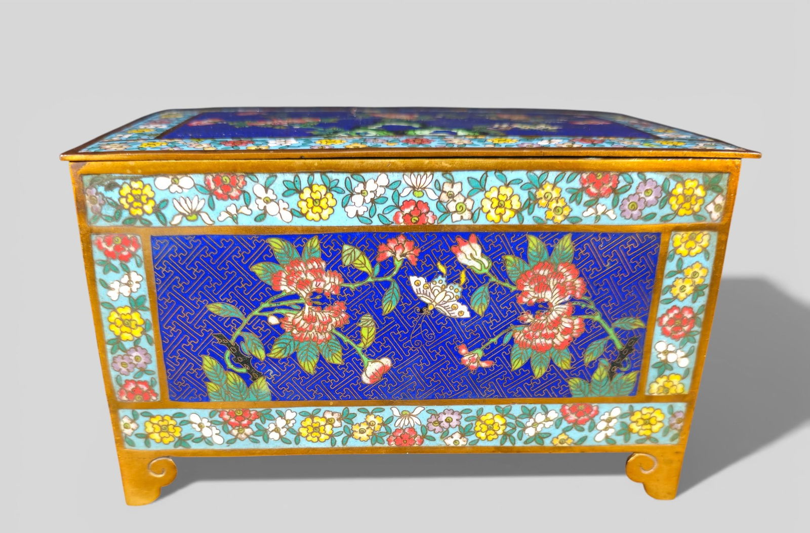 Cloisonné Enamel Hinged Lid Box Incised Qianlong Four-Character Mark: Cloisonné Enamel Hinged Lid Box Incised Qianlong Four-Character Mark. Rectangular; chrysanthemum decoration; single butterfly to front panel; blue ground with floral borders; scrolled gilt bronze