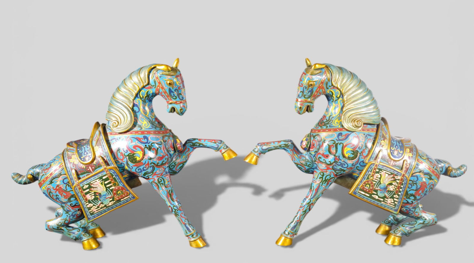 Large Chinese Cloisonne Enamel Horses: Large Chinese Cloisonne Enamel Horses. Pair. Mid 20th Century. Removable mane and saddle. Brass hoofs. Blue ground with vibrant color floral motif. 16 1/2 w x 5 1/4 d x 16 h.