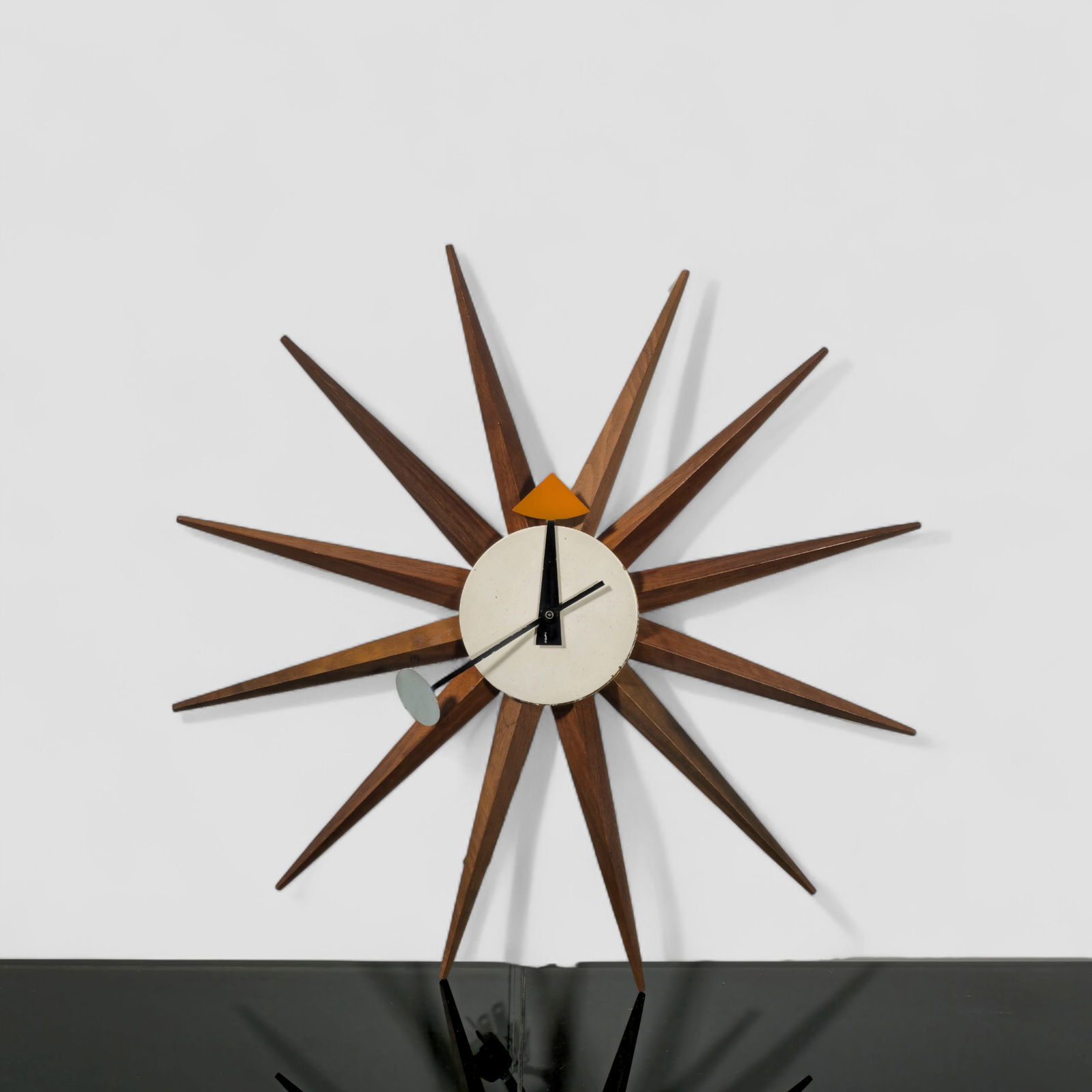 George Nelson & Associates Spike Clock: Mid-century starburst wall clock designed by George Nelson for Howard Miller, featuring radiating walnut spokes surrounding a circular enameled metal face. The clock displays Nelson’s signature