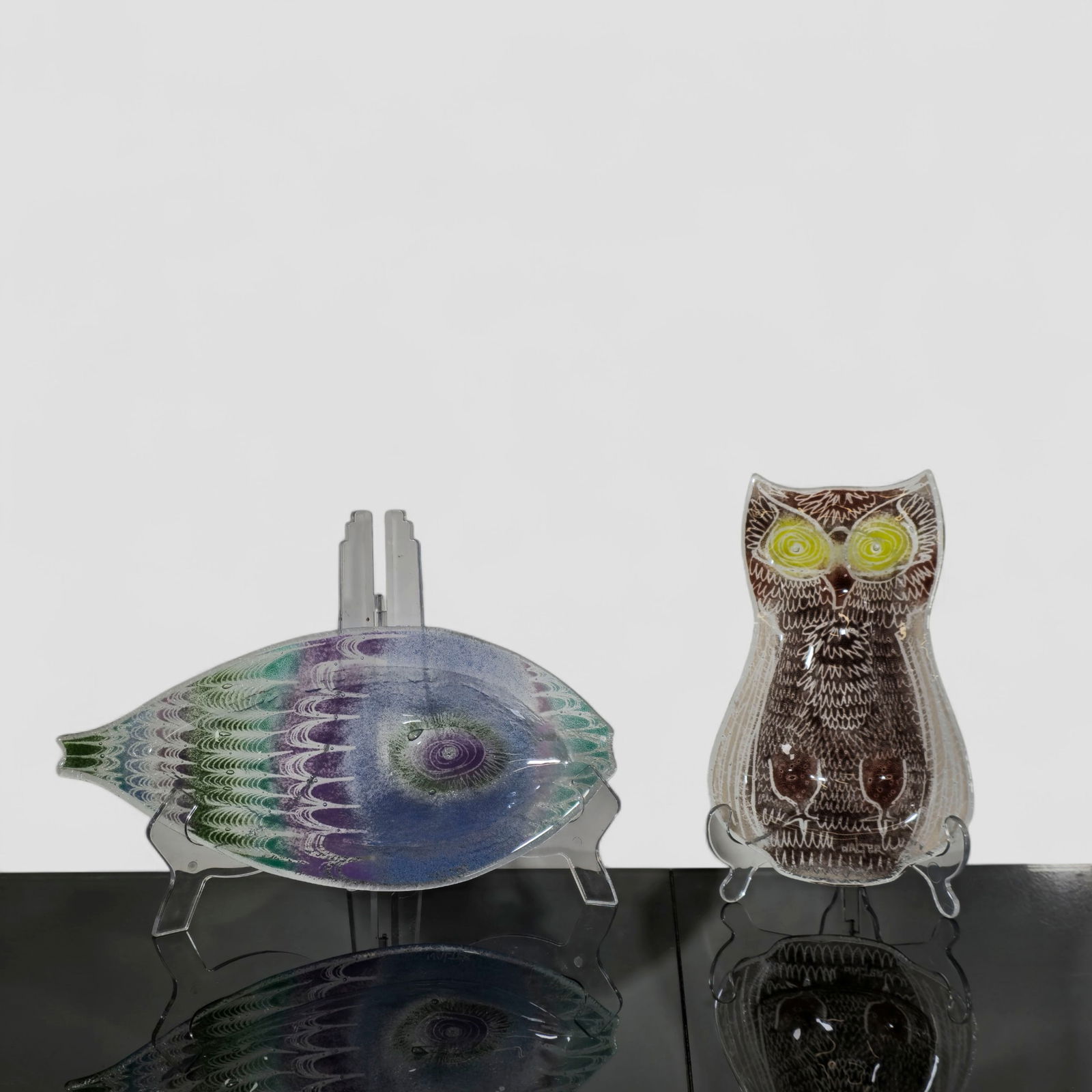 MCM Edwin Walter Glass Bowls: Group of two hand-decorated fused-glass dishes by American artist Edwin Walter, including an owl-form tray with bright yellow eyes and a fish-form dish in layered green, blue, and violet tones. Each