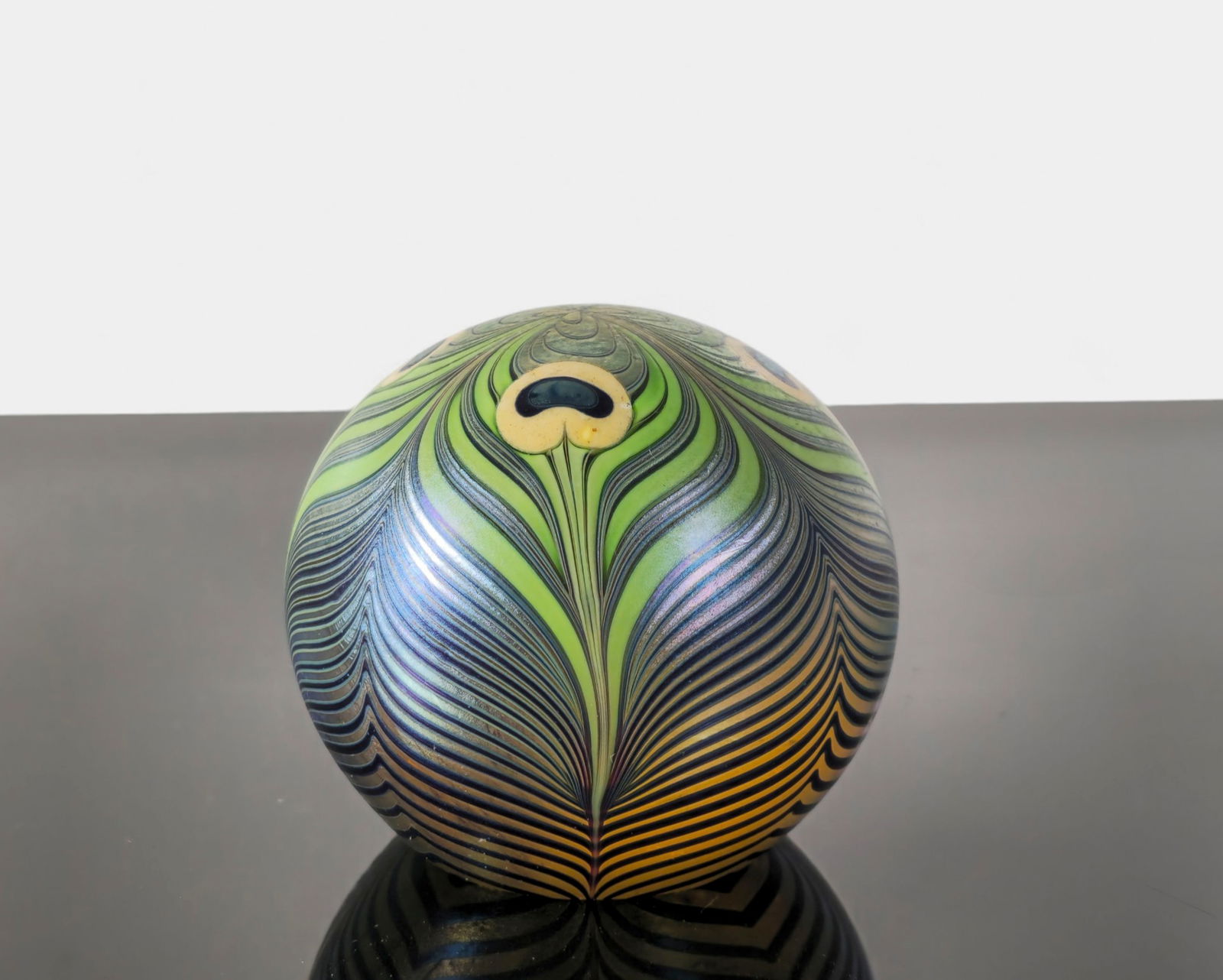 Orient & Flume Art Glass Paperweight: A signed Orient & Flume (Chico, California) iridescent art glass paperweight dated 1979, featuring a striking peacock feather motif in vibrant greens, blues, yellows, and purples. The surface
