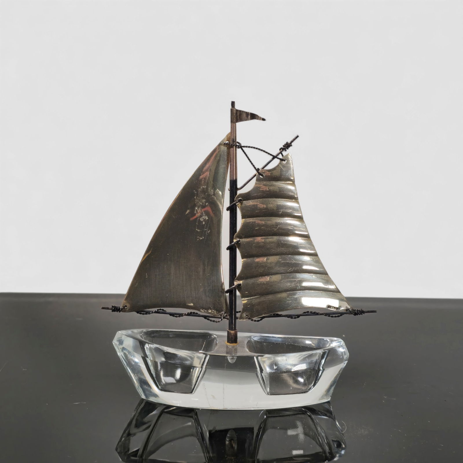 Sterling & Glass Sailboat Sculpture: German-made sterling silver and clear glass sailboat sculpture featuring hand-formed silver sails, rigging, and mast mounted to a solid faceted glass hull. Sails stamped STERLING and GERMANY. A