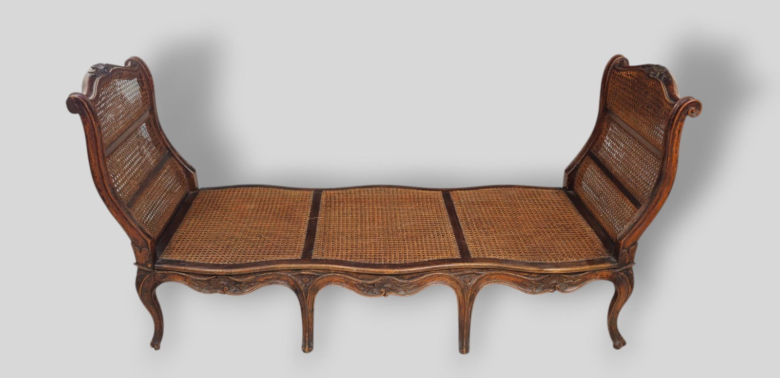 French Country Louis XV Bench: French Country Louis XV Bench or lit de repos. Circa 1870s. Walnut Scrolled and flared Sides with cane panels and seat. Scrolled aprons with high relief carved shells. Cabriole legs with carved floral