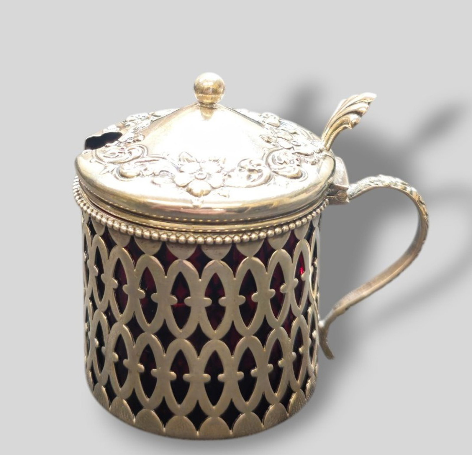 Sterling Silver and Ruby Red Glass Mustard: Sterling Silver and Ruby Red Glass Mustard. Hinged lid with hand chased floral border. Pierced body and loop handle. Original ruby red liner. Marked sterling and #112 to underside. 2 3/4w x 2d x 3h.