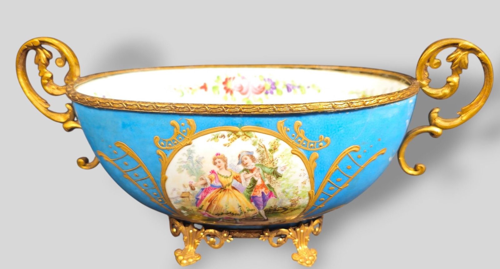 Sevres French Bronze Mounted Porcelain Center Bowl: Sevres French Bronze Mounted Porcelain Center Bowl. Circa 1890. Oval form with gilt scrolled handles. Decorated with Courting Couple on pathway. Gilt border and motif over a blue ground. Gilt base wit