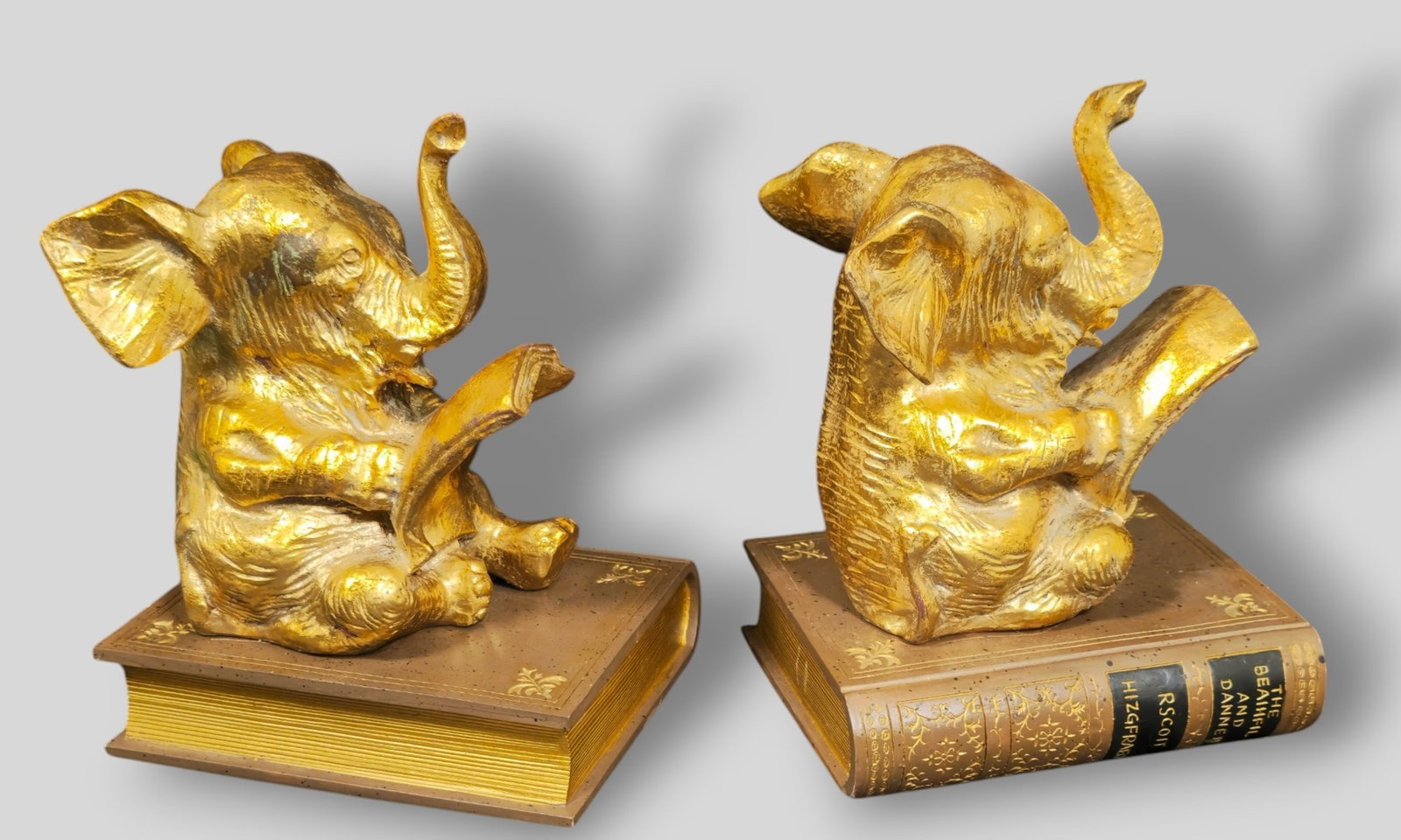 Gilt Elephant Reading Bookends: Gilt Elephant Reading Bookends. Pair. Elephant sitting reading a book raised on F Scott Fitzgerald tole and gilt metal book. 5w x 4d x 6 1/2h.
