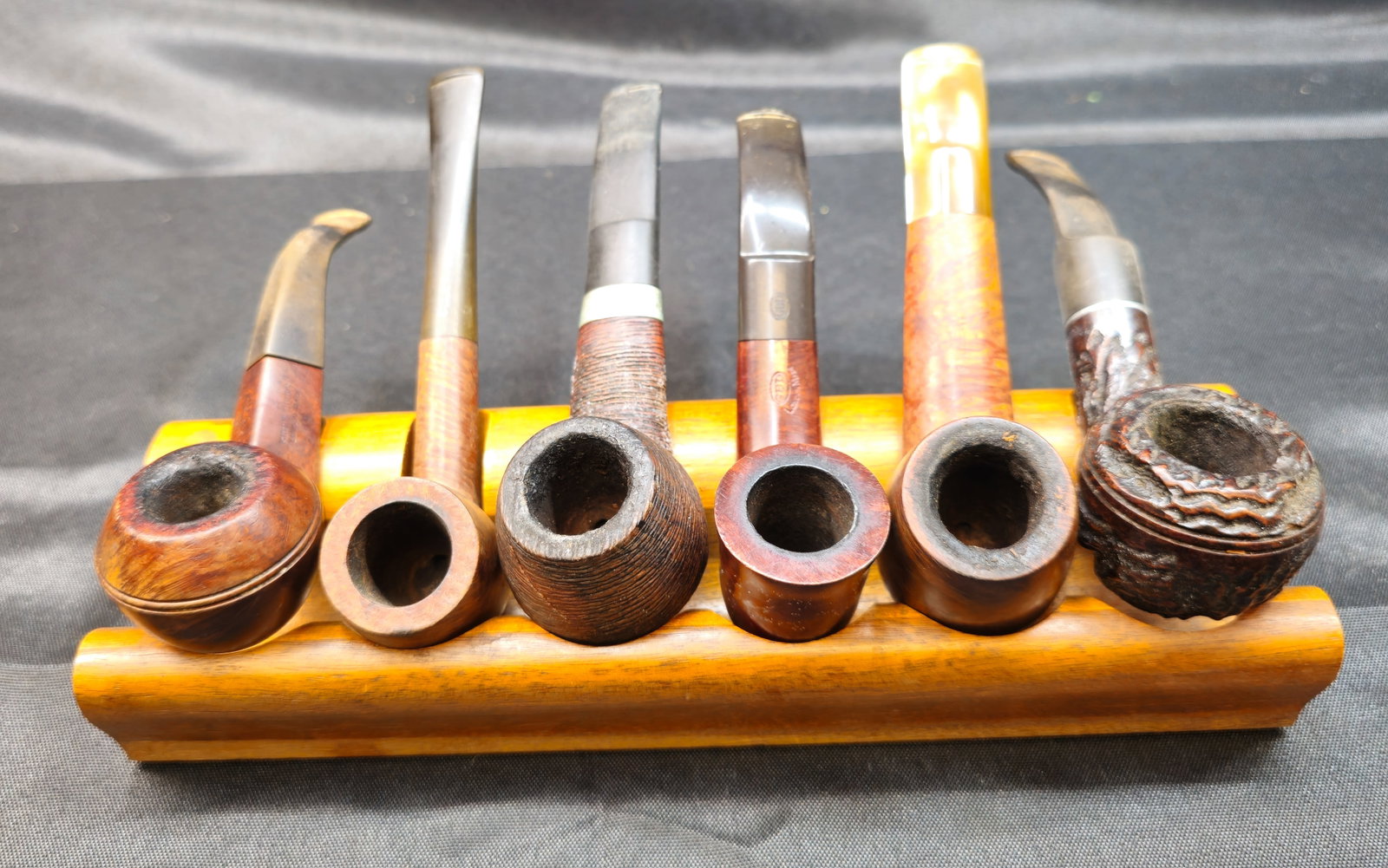 Six Smoking Pipes with Wooden Pipe Rack: Six Smoking Pipes with Wooden Pipe Rack. Assembled collection of six smoking pipes displayed on a fitted wooden pipe rack. The group features a varied assortment of classic forms with smooth,