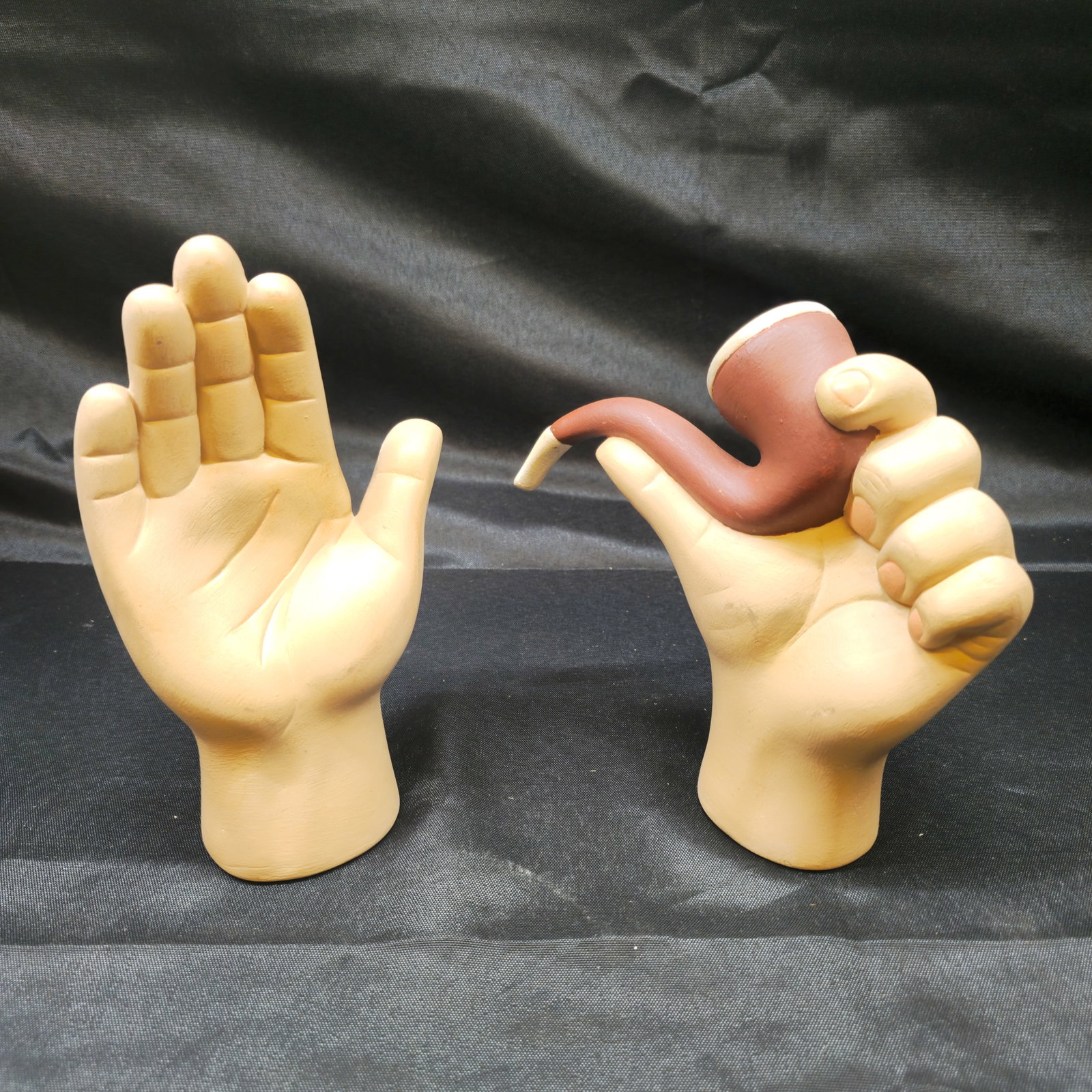 Pair of Surrealist Hand & Pipe Sculptures 1975: Pair of sculptural hand-form objects, comprising an open hand and a hand holding an oversized smoking pipe. Painted molded composition construction in flesh tones with brown and cream pipe