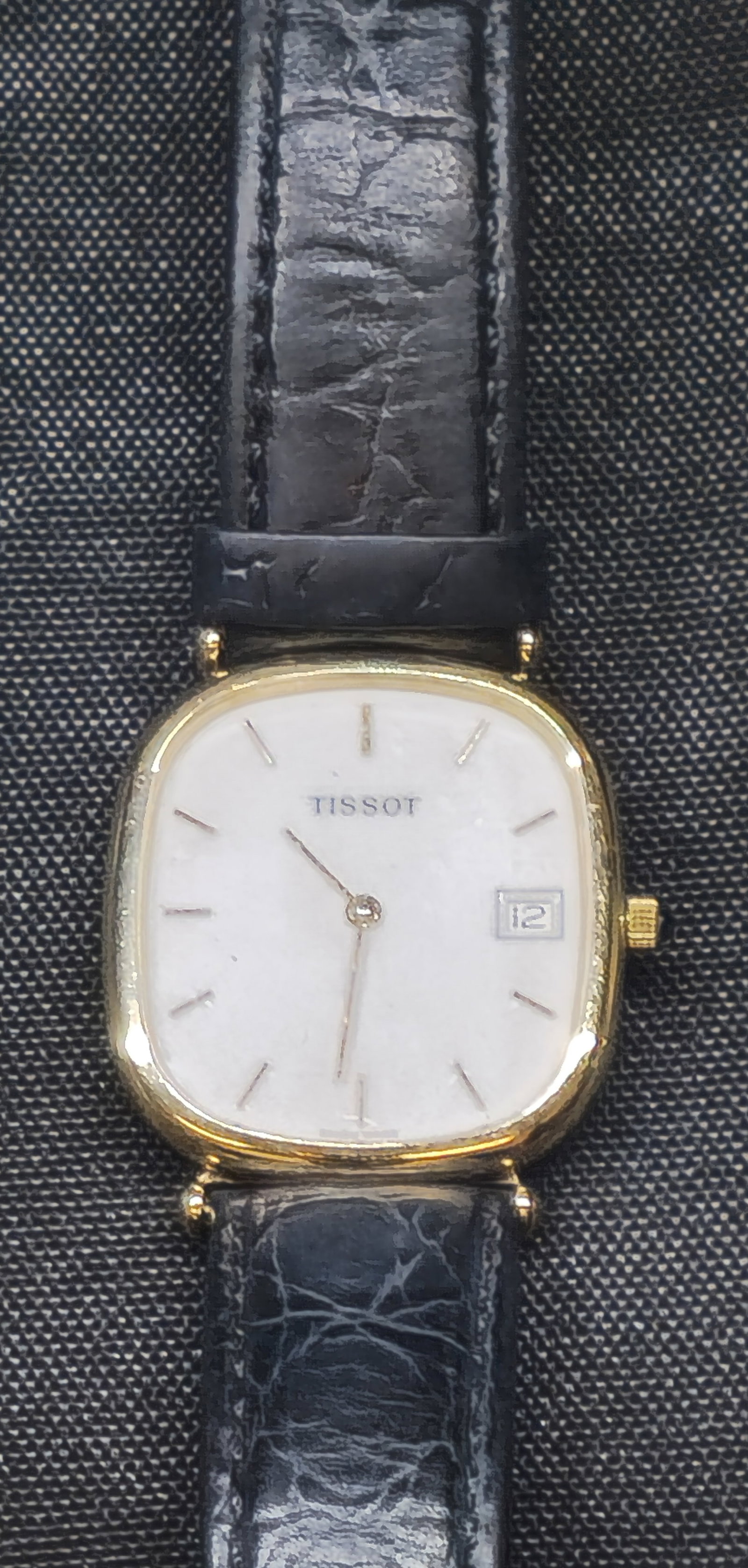 Tissot 14K Gold Swiss Wristwatch: Tissot Swiss wristwatch having a 14K yellow gold cushion-form case, silvered dial with applied baton hour markers, date aperture at 3 o’clock, and black leather strap. Case bearing Swiss squirrel go
