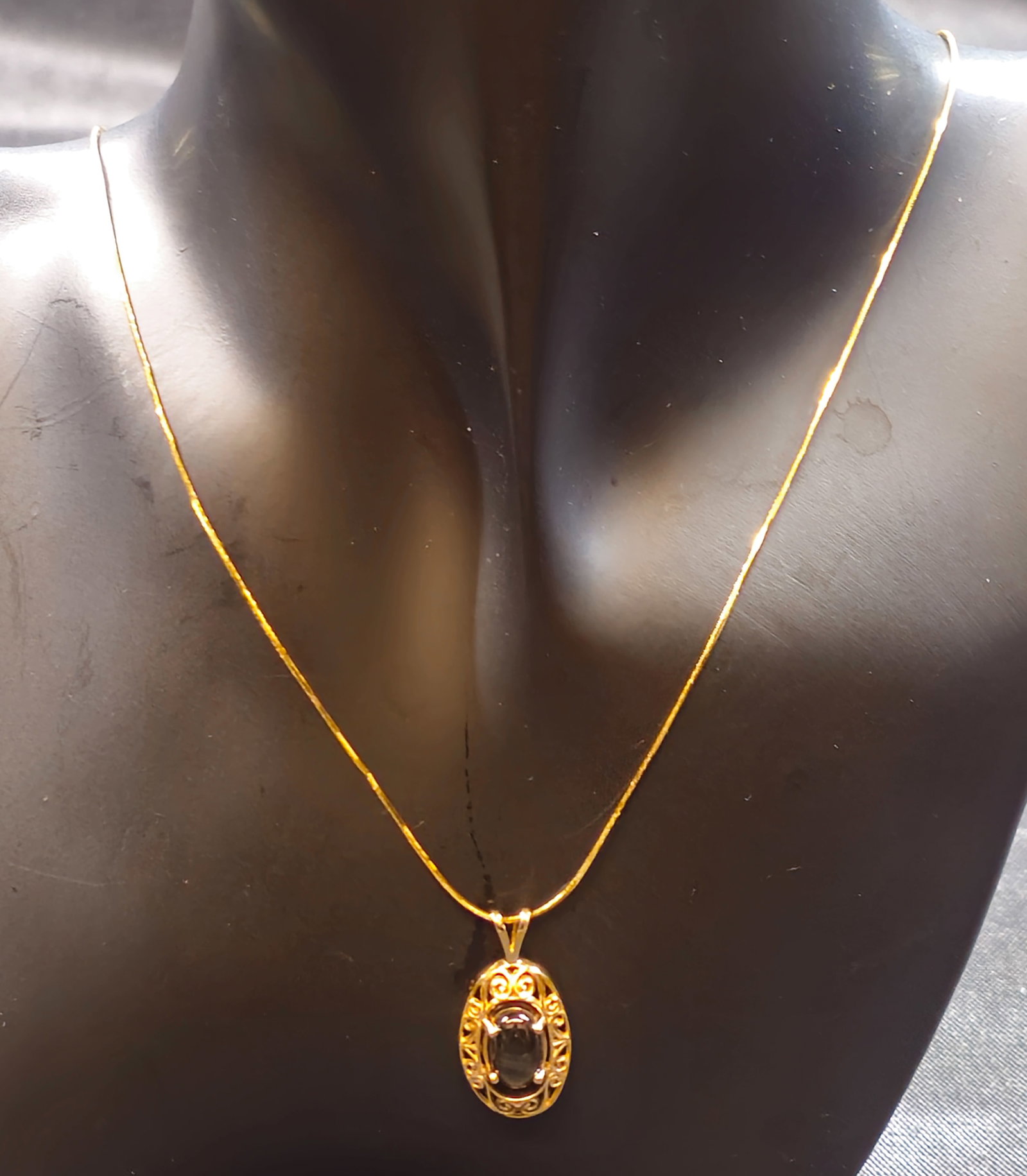 10K Gold Chatoyant Cabochon Pendant Necklace: 10K yellow gold necklace featuring an oval openwork pendant set with a dark oval cabochon displaying a pronounced star or chatoyant effect, suspended from a fine gold chain with spring-ring clasp.