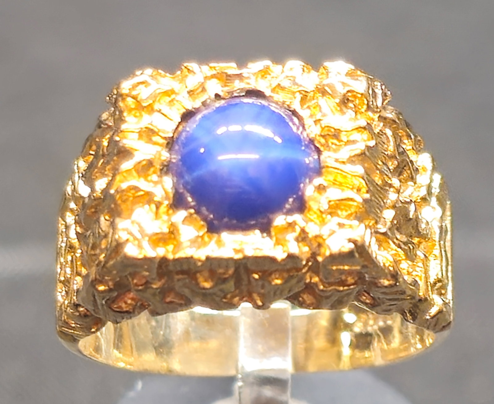 10K Gold Star Sapphire Ring: 10K yellow gold ring featuring an oval blue star sapphire cabochon in a raised setting, surrounded by an ornate textured gold mount with wide tapered shoulders. Interior marked "10K" with maker's mark