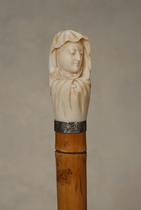 A lovely ivory cane of the Madonna: A lovely ivory cane of the Madonna. The elephant ivory handle is 2 2/3" high and 1 1/4" at its widest. It depicts a demure Virgin Mary with detailed facial features. She is draped in a loose cloak. Th