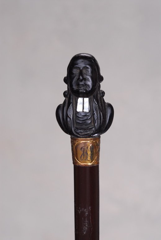 A very nice cane with a bust of John Wesley: A very nice ebony monkey cane cane. The ebony handle is 2" high and 1 7/8" at its widest. It depicts a monkey with yellow glass eyes and stark white teeth. His hair is neatly combed. There is a silver