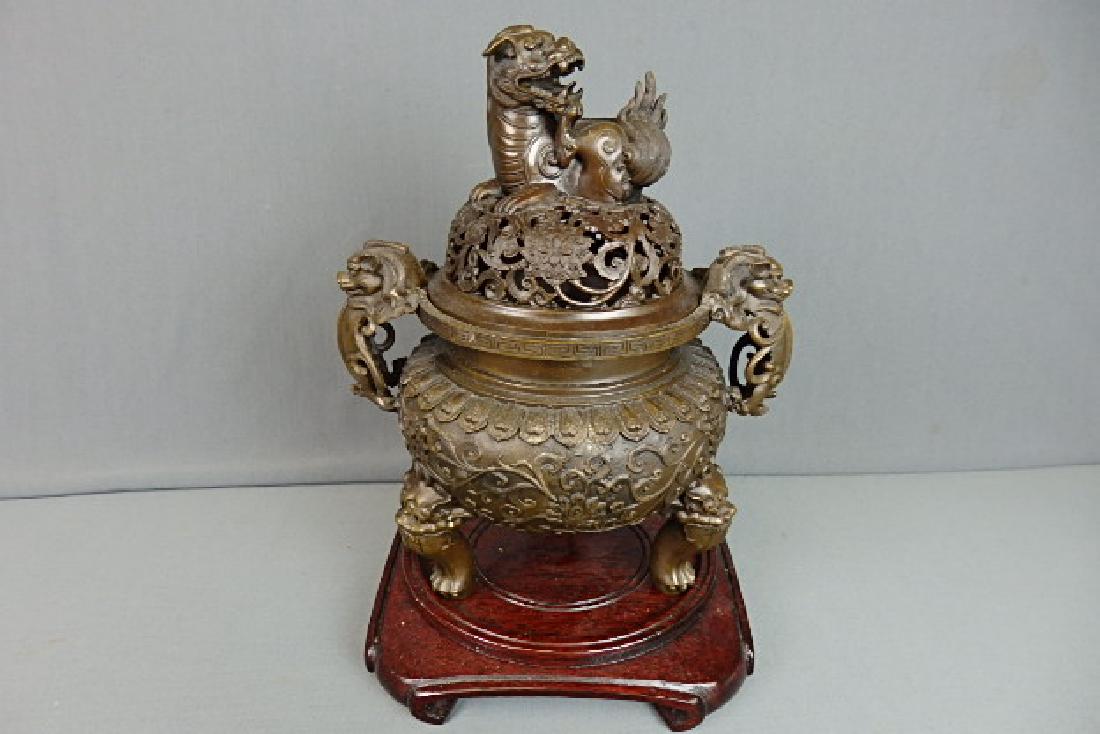 Chinese Bronze Incense Burner: Made out of bronze. Very heavy. Comes with a wooden base. 3 footed with dog like faces on top of the legs. Dogs for the side handles. Laying down foo dog on the top. With the lid on it is 11.5 inches 
