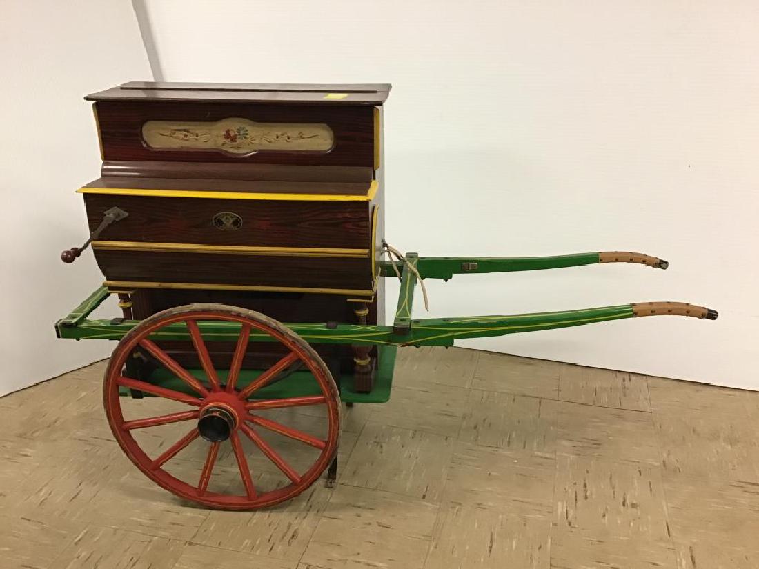 Hurdy Gurdy Organ Music Box: Labeled on front by maker "Vicente Llinares Faventia, Barcelona" with Made in Spain label inside, paint decorated crank music box organ, stands on green, red and yellow painted push cart. Measures 33 