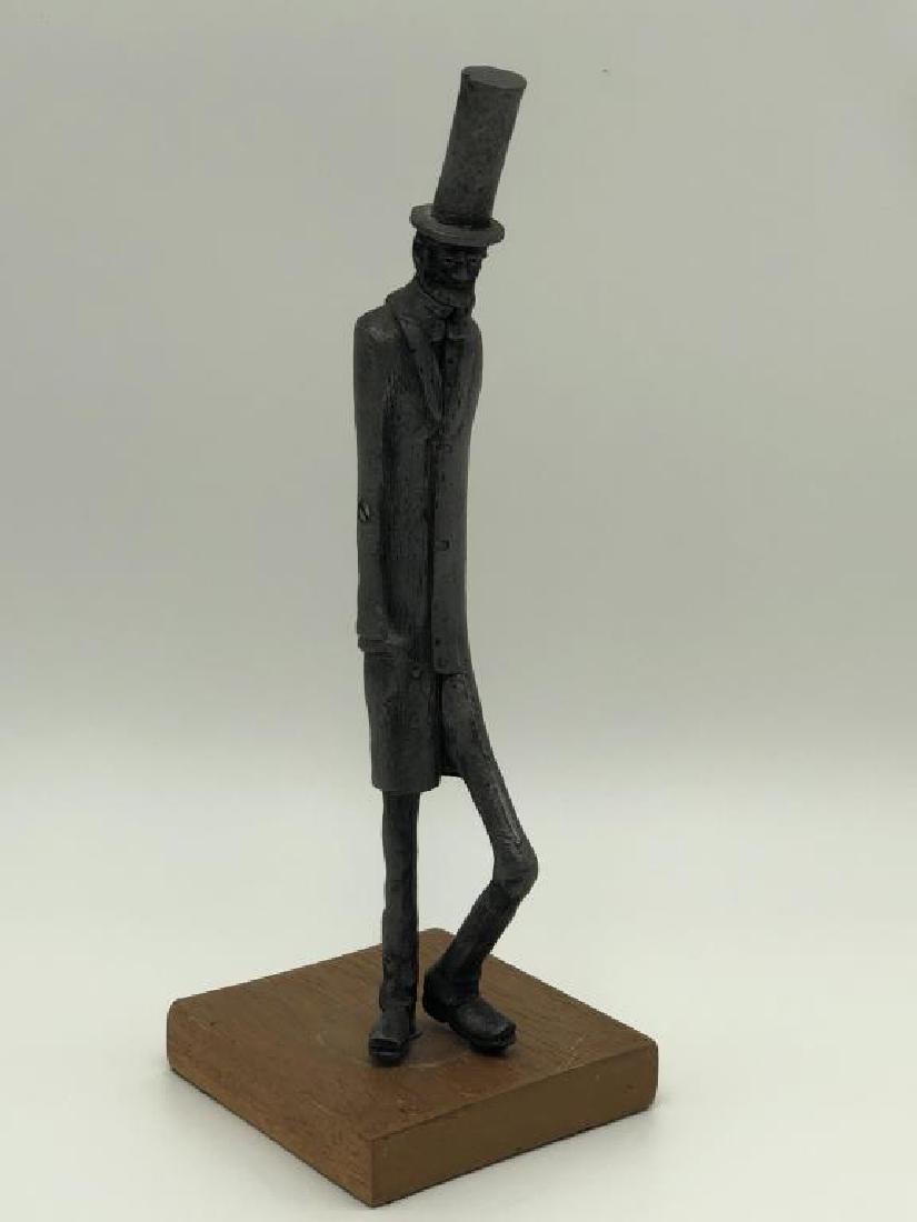 Pewter Abraham Lincoln Figurine: Character carving of Abraham Lincoln, exaggerated tall and thin form on wood stand. Part of cane is missing, measures 11 inches high, base is 4x4 inches.