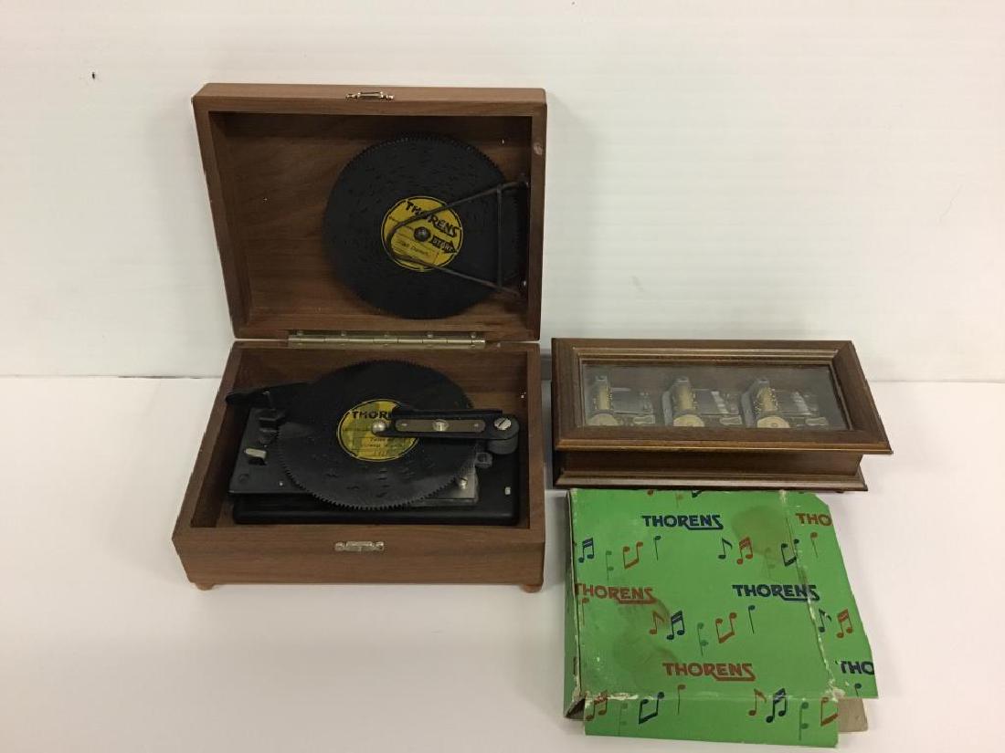 2 Swiss Music Boxes: Table top music box, wood case with clear plastic top, plays three songs using different dials on the bottom side, labeled "Reuge, Swiss Musical Movement" the song titles are "Edelweiss", "I'd Like to