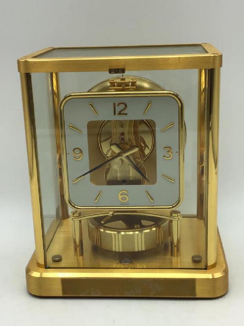 Atmos Swiss Mantle Clock: Gold plated mantel clock marked inside as "ATMOS by Jaeger Le Coultre, Thirteen (13) Jewels, Swiss." Measures 9 inches high by 7 1/2 inches wide by 6 inches deep, clock is running, each lower corner o