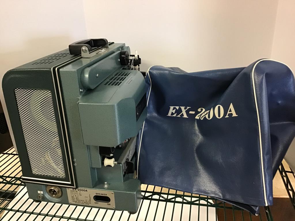 EIKI EX-2000A Film Projector: EIKI projector, model eX 2000A, serial number A 4860. Made in Japan. Comes with protective cover. May be missing some wires/cable. Measures approximately 14 inches high by 14 inches wide by 11 1/2 inc