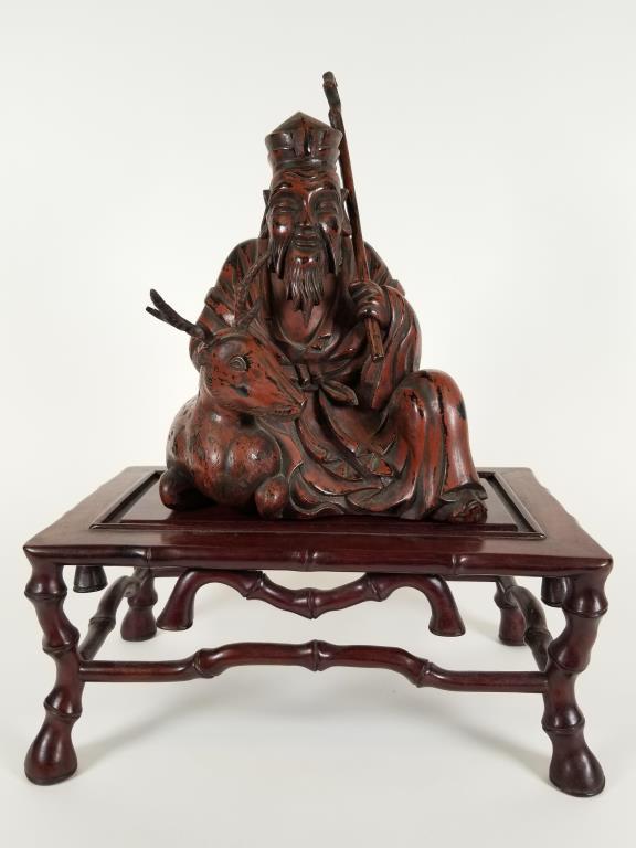Carved Wooden Seated Immortal with teakwood base hand: hand carved wood, reddish paint, reclining animal, figure is 9 inches tall x 8 inches wide by 6 inches deep, comes with a separate teak wood stand, 5.5 inches tall x 12 inches long x 8 inches wide. Ho