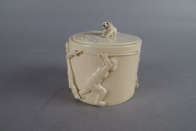 Ivory Box with Lid: 3" H x 3.25" D ivory box with lid; lid decorated with lion & cub atop, small triangular loss to outside edge of lid; circumference depicts two African males with pointed spears hunting full body lion.