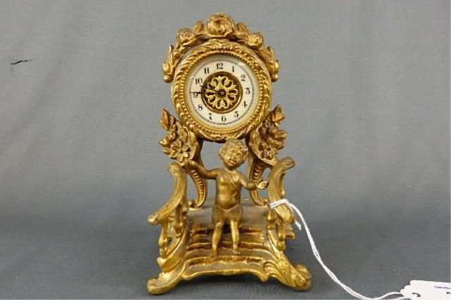 Figural Clock: 5.75" T Waterbury Clock Co. figural clock, brass figure of a putti seated on stairs, white enamel clock face, crack in clear outer clock face case.