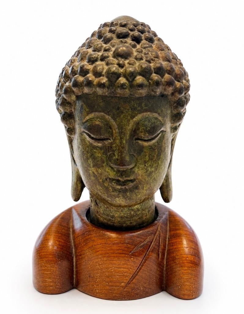 Decorative Vintage Buddha Bust: Decorative Vintage Buddha Bust. This lot includes one (1) metal Buddha head displayed on one (1) wooden chest-form stand. When assembled, the piece measures approximately 6.25" in height and