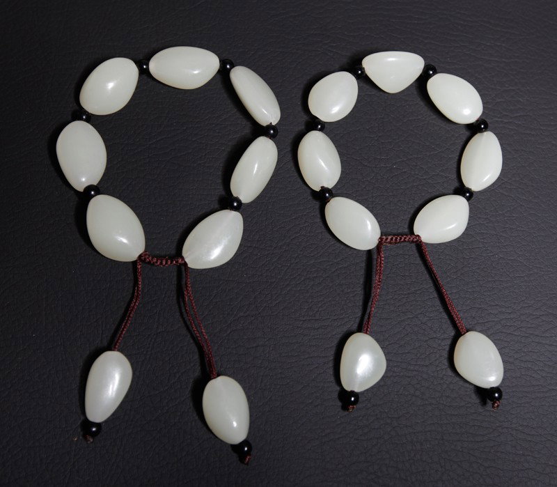 PAIR OF WHITE JADE BRACELETS: Each with 7 beads separated by darker beads and tassel beads on the end.