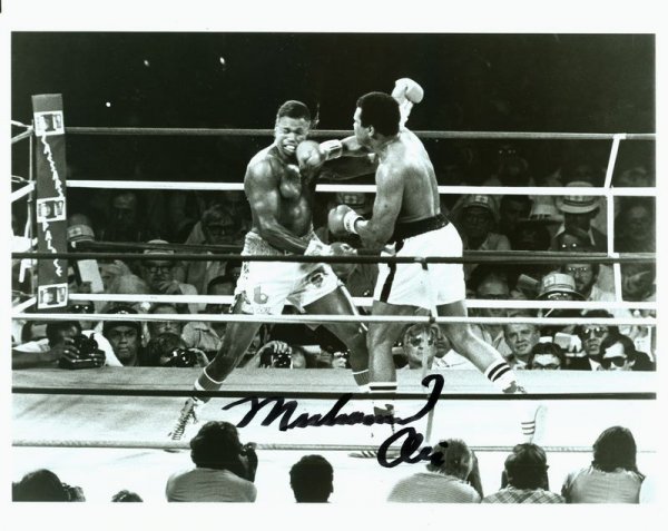 MUHAMMAD ALI SIGNED PHOTOGRAPH: 952. MUHAMMAD ALI SP, b/w, 10"x8" action still as he strikes a blow to opponent Larry Holmes (1980), the only fight Holmes lost by anything other than a decision. Large signature, bol
