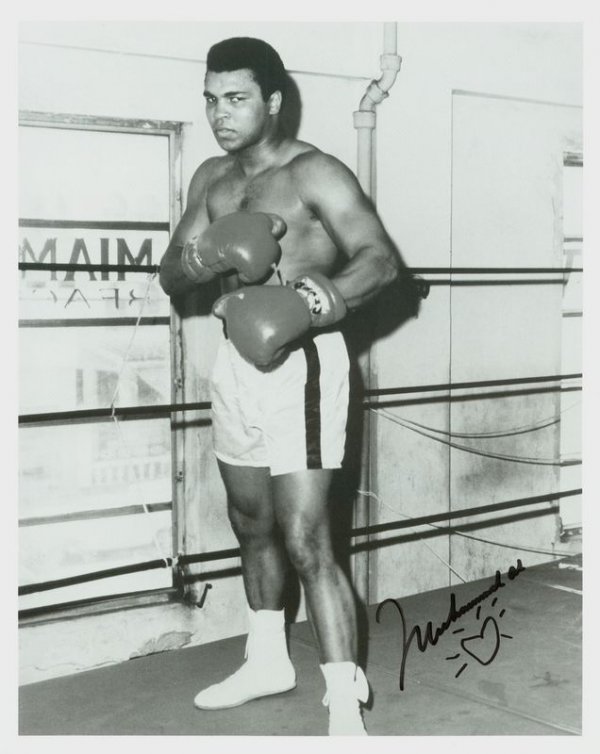 MUHAMMAD ALI SIGNED 5TH STREET GYM PHOTOGRAPH: 1121. MUHAMMAD ALI SP, b/w, 8"x10" full-length standing portrait in front of the window of Angelo Dundee's famous 5th Street Gym in Miami, FL, where Ali trained. Darkly signed in felt tip, ca. 1990s, 