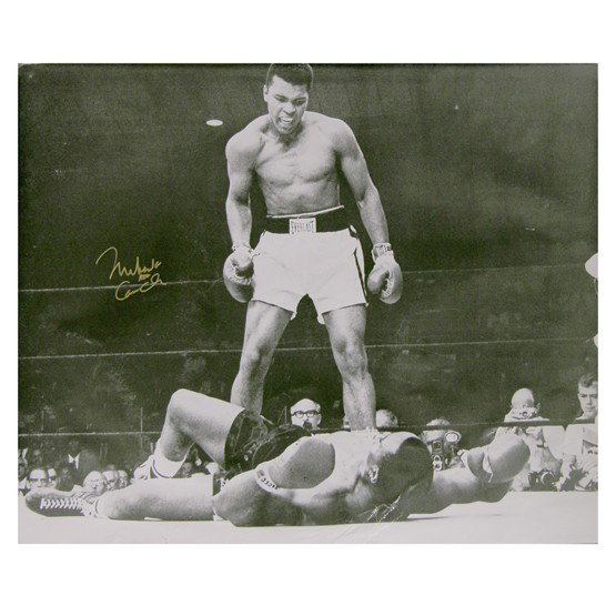 MUHAMMAD ALI: SP, b/w, 20"x16", action still of victorious Ali standing over a defeated Sonny Liston. Boldly signed with gold felt tip "Muhammad Ali aka Cassius Clay." Creasing at bottom edge extending into lower p