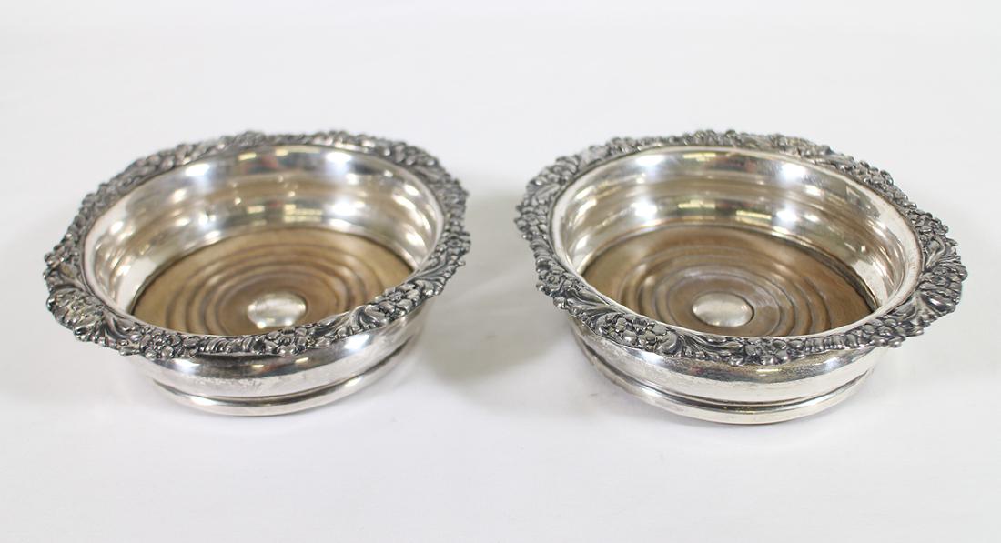 (2) ANTIQUE WINE COASTERS: Two antique silverplate wine bottle coasters with floral rims. Inside 5" wide, outside 6.25" wide.
