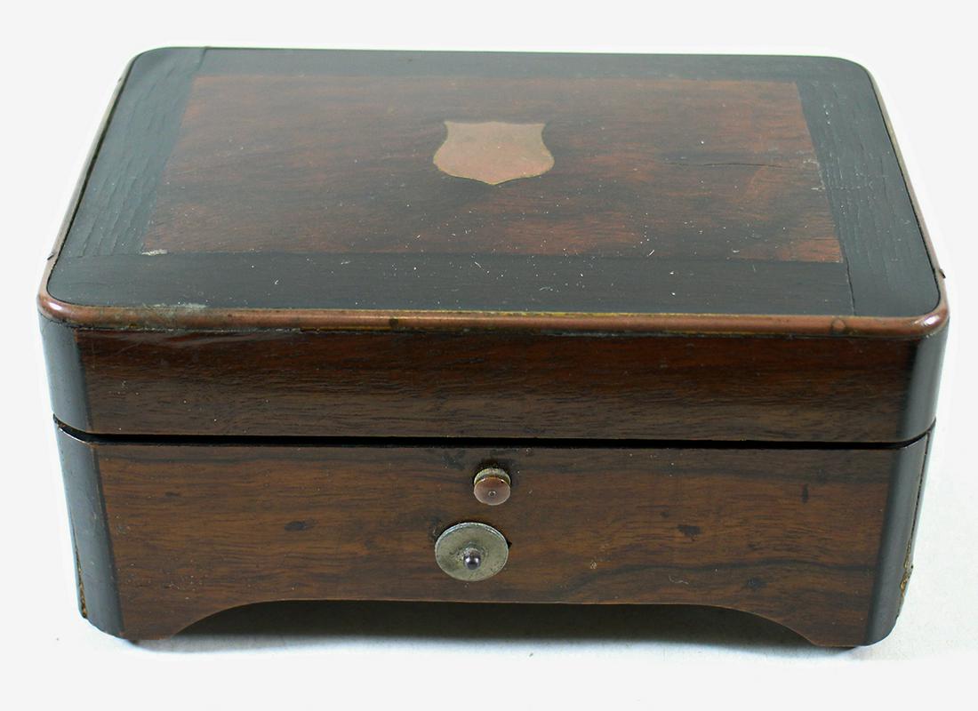 ANTIQUE WOOD CRESTED CYLINDER MUSIC BOX: A wooden box with a inlaid non monogrammed crest on top. The movement is marked Pat MSH 1st, 1881. It is working and comes with a key. It measures 5 1/4" x 3 1/2".