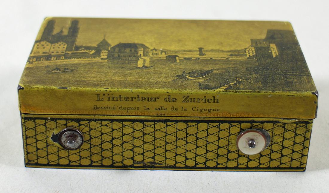 ZURICH METAL CYLINDER MUSIC BOX: An antique metal cylinder music box with a scene of Zurich on the top. The side of the box is marked L'interieur de Zurich dessine'depuis la sallede la Cigogne. It is working, no key. No visible marki