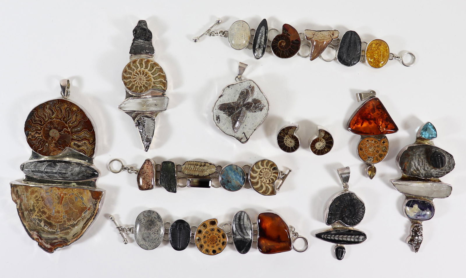 CHARLES ALBERT FOSSIL AMMONITE STERLING JEWELRY: A collection of fossilized jewelry by Charles Albert to include a very large pendant (5.5" x 3.3"), (3) bracelets, (5) pendants and a pair of earrings. Charles Albert jewelry is made of natural stones
