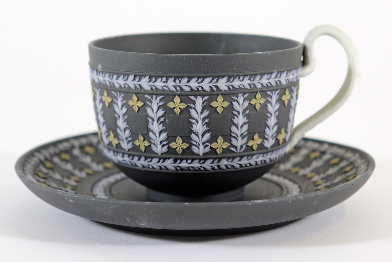WEDGWOOD TRI COLOR BASALTWARE TEACUP & SAUCER: An early Wedgwood black tri-color diced tea cup with saucer with a black background, white handle, white and yellow foliate design. The saucer measures 5 1/4" and the cup is 2 1/4" tall.