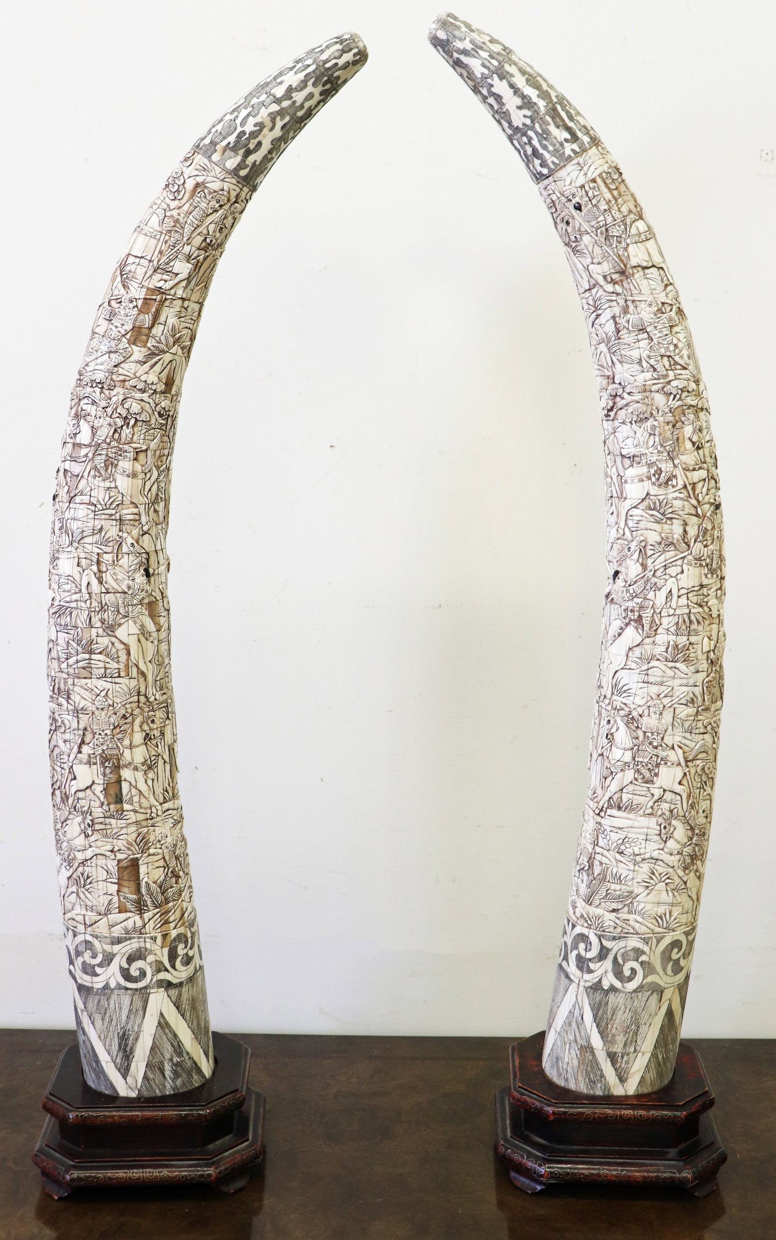 (2) CHINESE HAND CARVED BONE TUSKS, LARGE: A pair of Chinese relief bone tusks, on octagon shaped bases. Hand carved depicting intricate landscape and battle scenes on horseback. Measures 38" tall, wooden base is 3 1/2" x 7" x 6" .