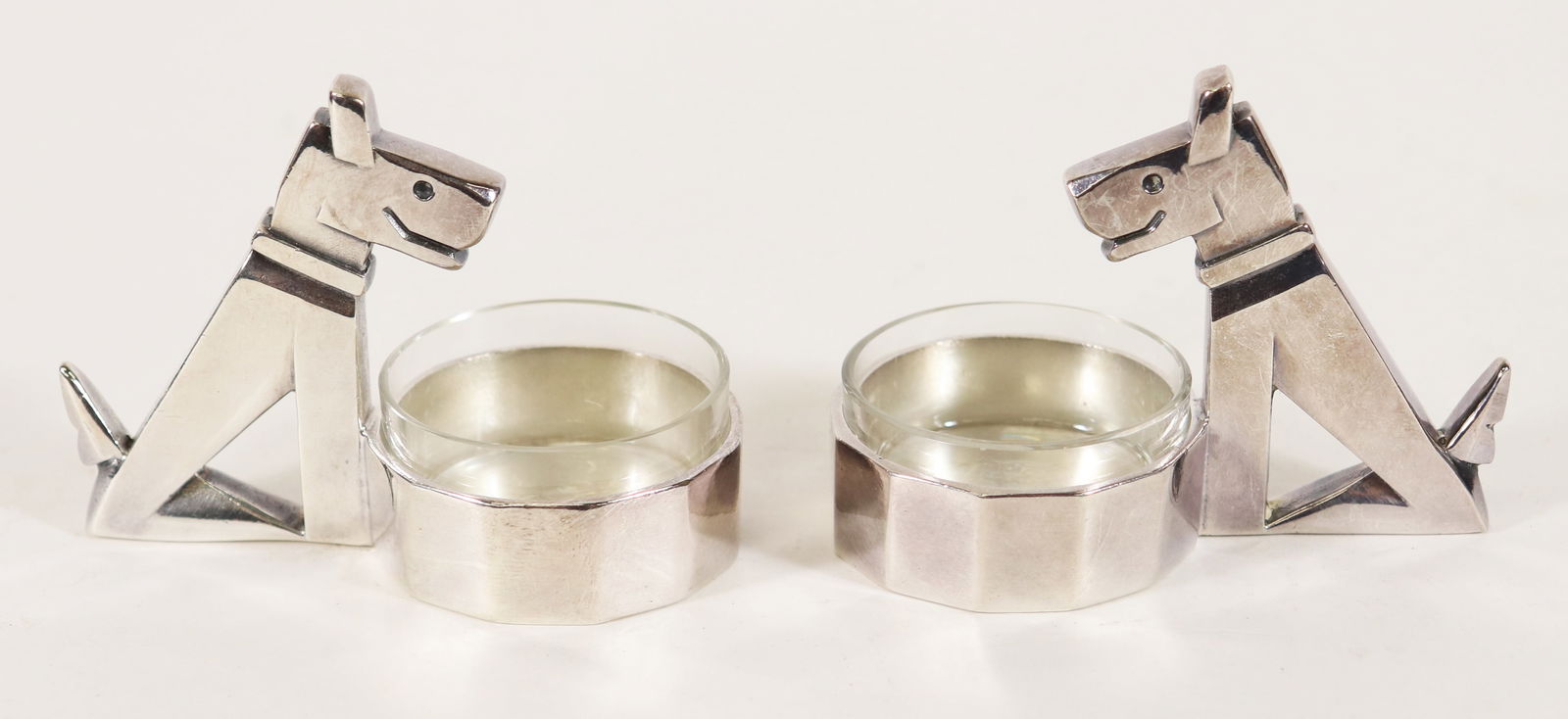 PAIR OF CHRISTOFLE RIC & RAC TERRIER SALT CELLARS: A pair of Christofle Gallia Art Deco style dog salt cellars, each with glass liner in the bowl in front of a seated terrier dog, and marked on bottom. Measures 2" x 3 1/4" x 1 1/2". From the Andrew Cu
