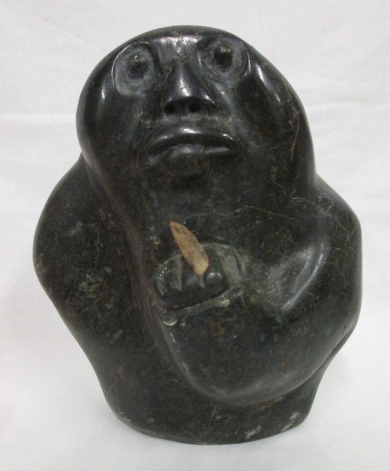 DOUBLE SIDED INUIT CARVING: Man with tongue sticking out and holding knife (or holding up middle finger?) some marks on bottom - possibly signed, reverse shows man holding oval object. Stands 9" tall 7 1/4" wide.