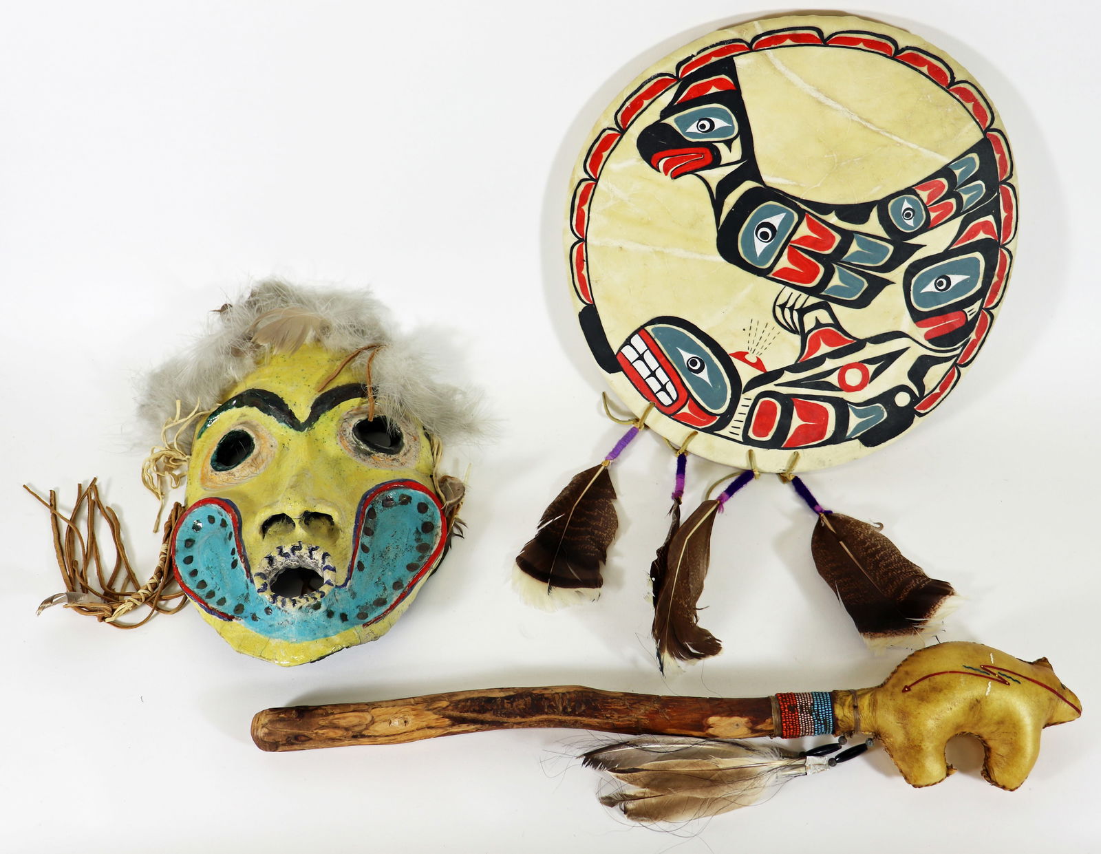 (3) ALASKAN TLINGIT CEREMONIAL PIECES: Three Alaskan Tlingit ceremonial pieces include a hand painted ceramic mask, with feathers, measures 15" x 22" x 3", a rattle stick with raw hide bear, beads and feathers attached, measures 15" x 10"