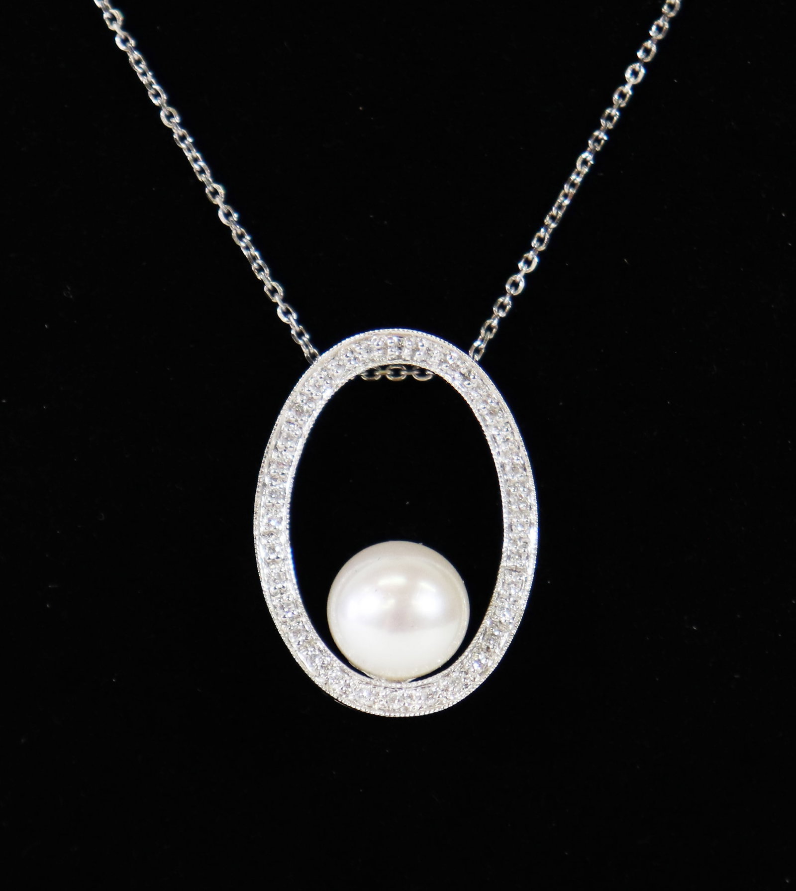 14K PEARL & DIAMOND OVAL PENDANT NECKLACE: 14KT White gold oval open pendant featuring a large round pearl accented with diamonds. Pendant measures approximately 1" long and includes a 19" 14K white gold chain. Total weight 5 grams (3.2 DWT).