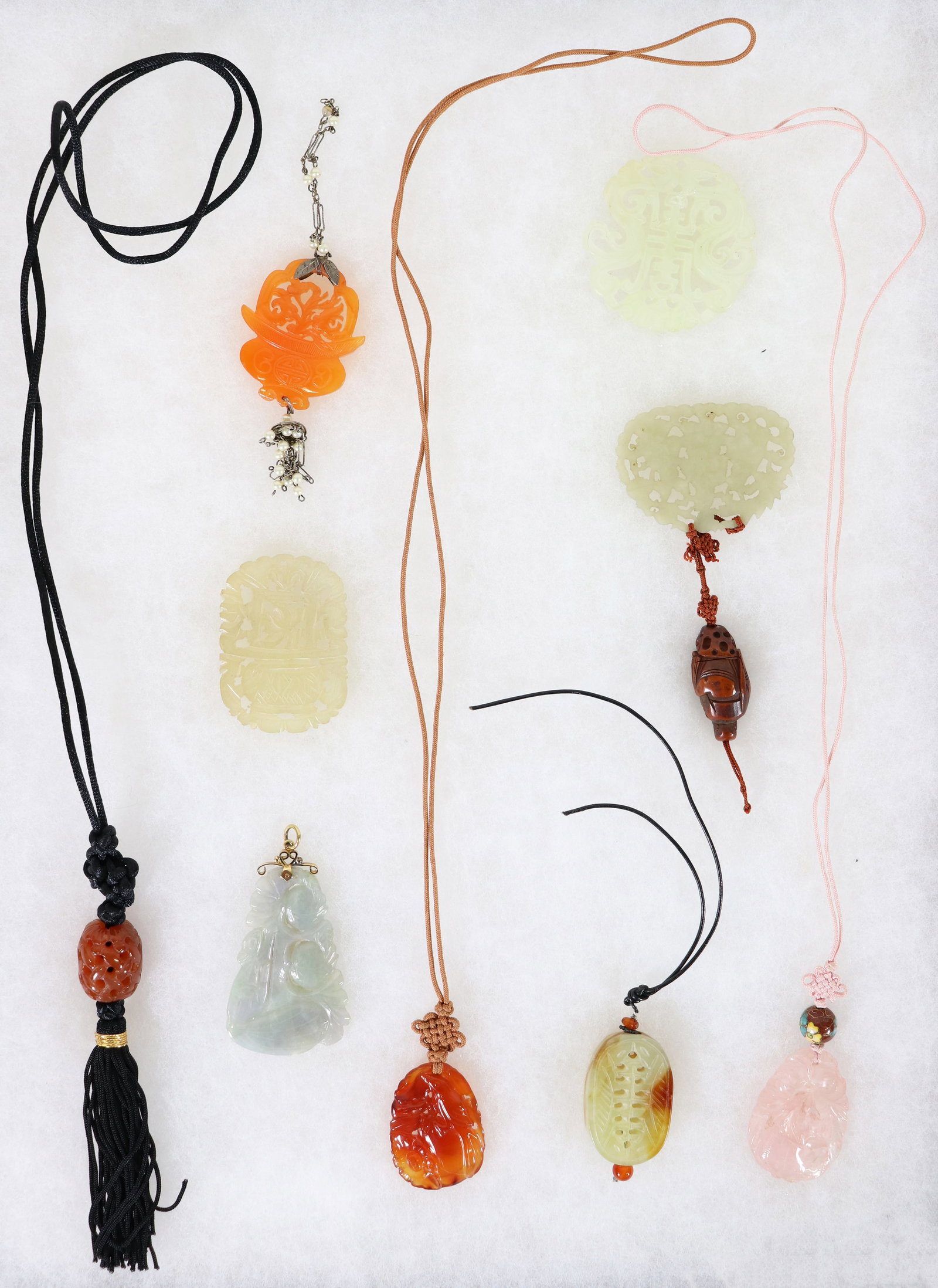 9 CHINESE PIERCED JADE PLAQUES: A collection of carved jade / jadeite / carnelian open weave pendants and plaques. Includes a jade pendant with a 14K yellow gold bale, an openwork plaque with a carved wood netsuke, a carnelian penda