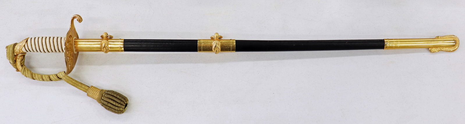 US NAVY OFFICERS PRESENTATION SWORD & SCABBARD: A US Naval Officer's ceremonial dress sword with knot and scabbard. It is marked Boston Uniform Co Germany. It comes with the case made by Hilborn Hamburger Inc. It measures 34" long.