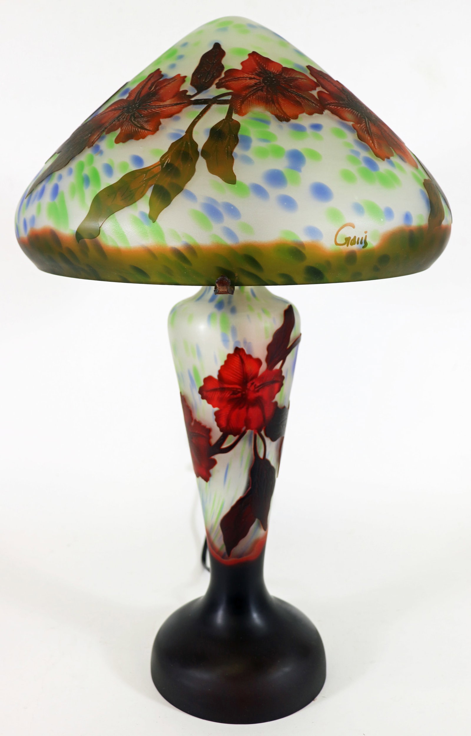 GALLE STYLE CAMEO GLASS TABLE LAMP: Emile Galle style cameo glass table lamp with red and black large blossom floral design set against blue and green splatter colors. Measures 23" tall with shade 13" at is widest, base is 7".