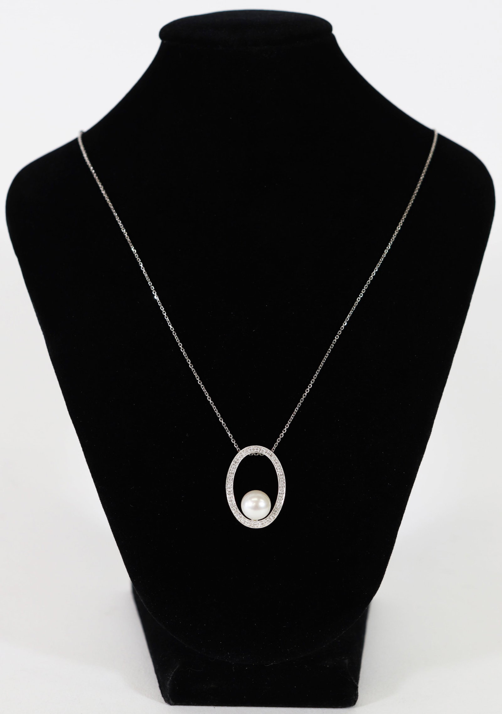 14K PEARL & DIAMOND OVAL NECKLACE: 14KT White gold oval open pendant featuring a large round pearl accented with diamonds. Pendant measures approximately 1" long and includes a 19" 14KT white gold chain. Total weight 5 grams (3.2 DWT).
