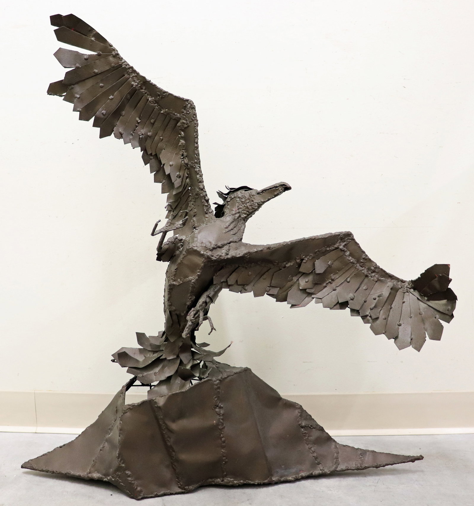 BRUTALIST METAL BIRD SCULPTURE: A large welded metal bird of prey sculpture depicting a bird in mid flight (or landing) with outstretched wings and detailed talons extending forward. Base is drilled to attached to wall. Signed by Ar
